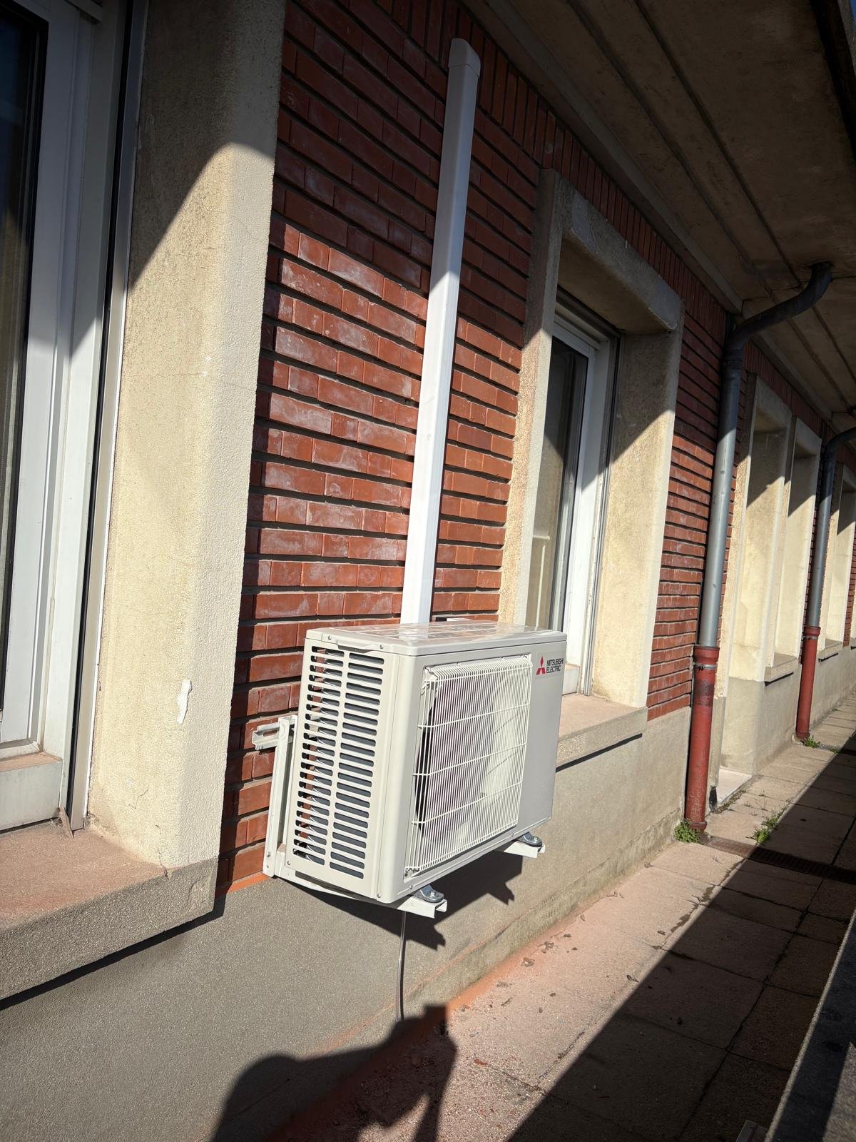 Unité extérieure Mitsubishi Electric posée en façade brique avec sectionneur rouge